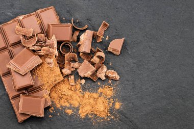 Çikolata parçaları ve çikolata talaşı karanlık bir arka plan üzerinde kırık. Metniniz için boşaltmak ile üstten görünüm.