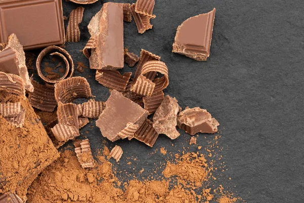 Broken chocolate pieces and cocoa powder on a dark background. Top view.