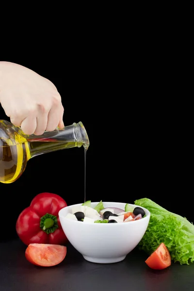 vegetable salad with olive oil pouring from a bottle.