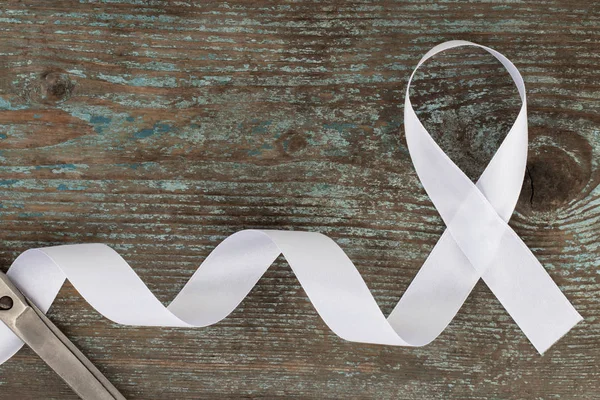 white ribbon on the wooden background with copy space. White or light pearl color ribbon for raising awareness on Lung cancer, Bone cancer, Multiple Sclerosis, Severe Combined Immune Deficiency Disease (SCID) and Newborn Screening  symbol.