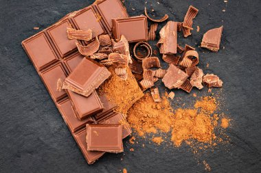 Kırık çikolata parçaları ve karanlık bir arka plan üzerine kakao tozu.
