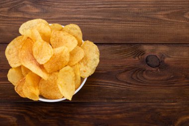 Ahşap arka plan üzerinde kase gevrek patates cipsi. Üstten Görünüm ile 