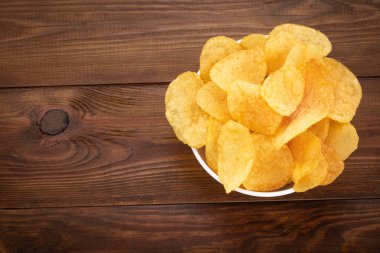 Ahşap arka plan üzerinde kase gevrek patates cipsi. Üstten Görünüm ile 