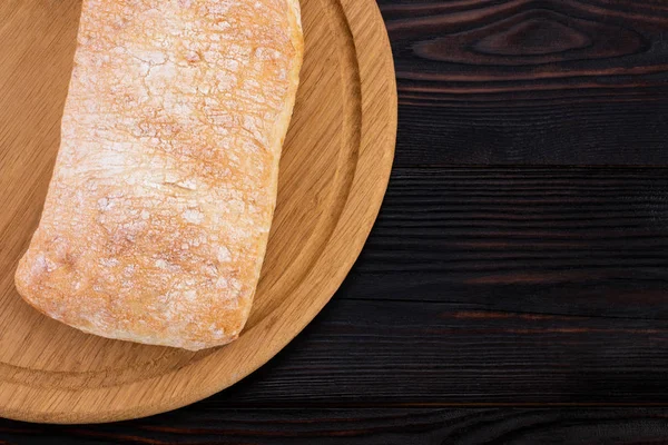 Ciabatta na płycie do krojenia na ciemnym drewnianym stole, Top — Zdjęcie stockowe