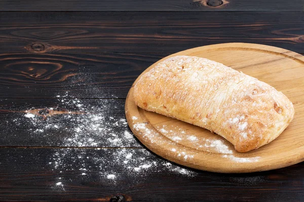 Pão de ciabatta em uma tábua de corte na aba de madeira escura — Fotografia de Stock