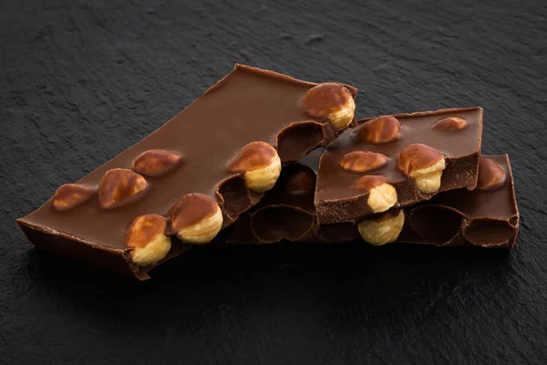 Pedaços de chocolate de leite com nozes em um fundo escuro — Fotografia de Stock