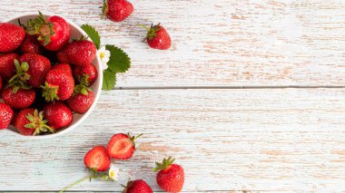 Beyaz ahşap masada fotokopi alanı olan bir kase taze çilek. Üst görünüm.