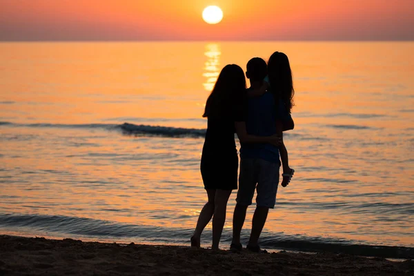 Baba, anne ve kızı denizde güneşin doğuşunu izliyorlar. Aile tatilde..