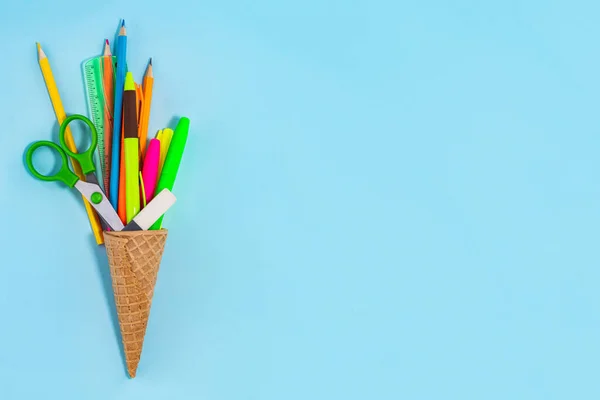 青い背景に学校用品でいっぱいのアイスクリームコーン コピースペース付きワッフルコーンの様々な文房具 教育と学校の概念に戻る — ストック写真
