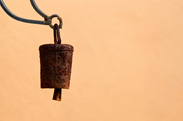 An old rusty metal bell is hanging suspended in air outside against a blank tan wall background, with copy space.