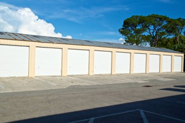 Çoklu birim veya multi-bay garaj görünümünü yazın depolama Florida'da terk edilmiş büyük ağaç ve bulutlar ve kırık driveway ile parlak ışığında binada. Metal çatı zarar görmüş ve paslı eski,.