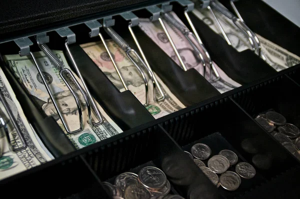 A retail cash drawer in open displaying various types of US currency money with shallow depth of field. Grain visible at 100%