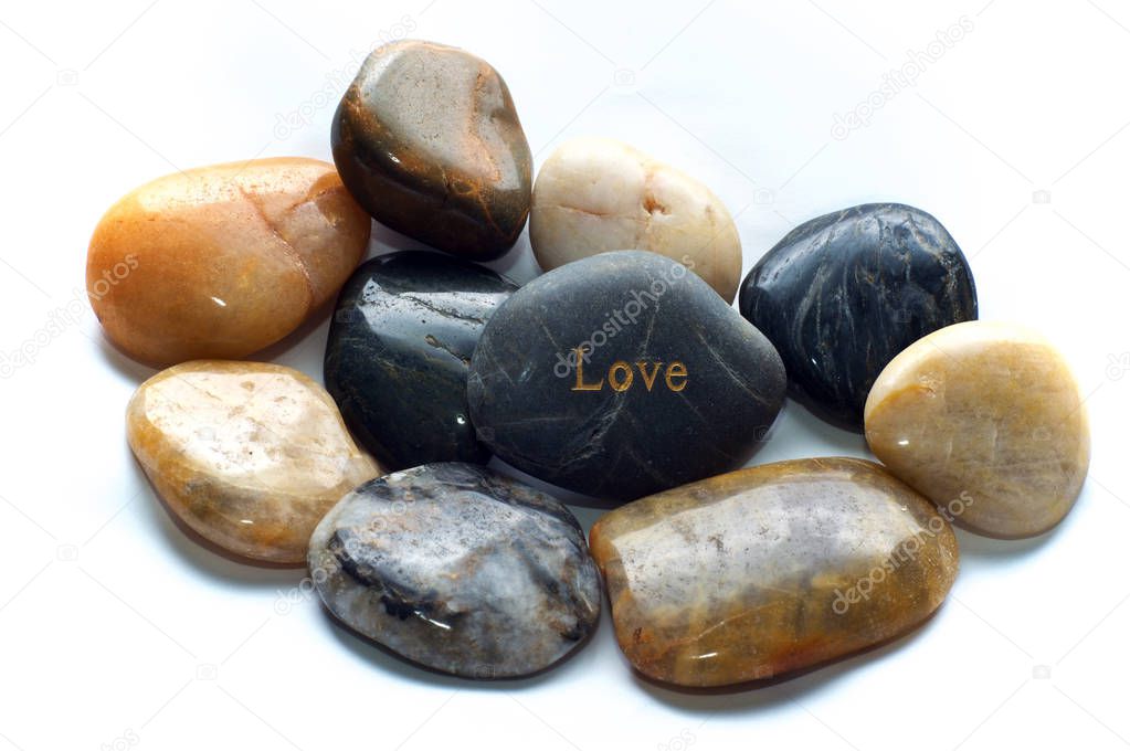 A gray polished river stone with the word love on it surrounded by many other rocks. Over white, not isolated.