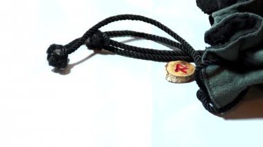 Yavaş çekim hızı kullanarak kaydedilen, İpli çanta sağ tarafta ve el oyma ahşap viking runes yukarıdan düşmüş gibi sihirli bir şekilde beyaz arka plan üzerinde görünmesini.