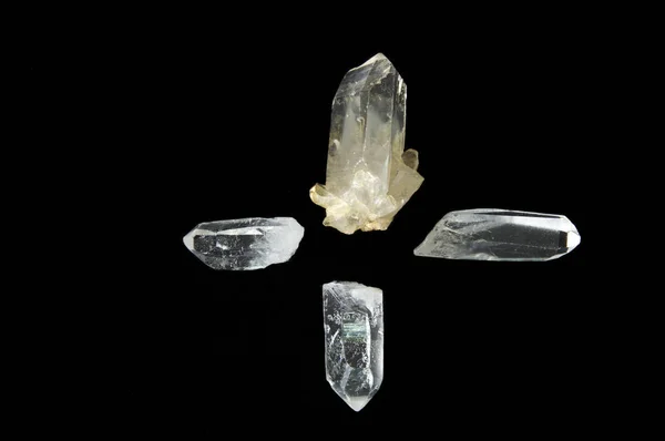 Four clear quartz crystal points on black background, one pointing in each direction forming a cross.