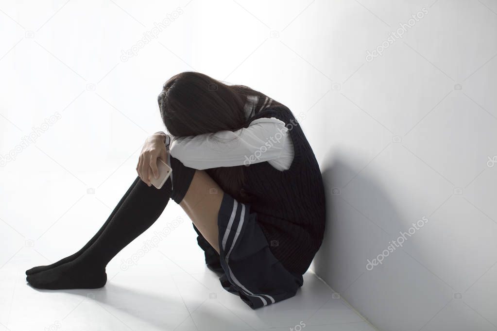 sad teenager student holding mobile phone and sitting on the floor