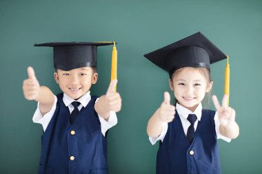 Mutlu çocuk ve başparmak gösterilmesini mezuniyet şapkalı kız