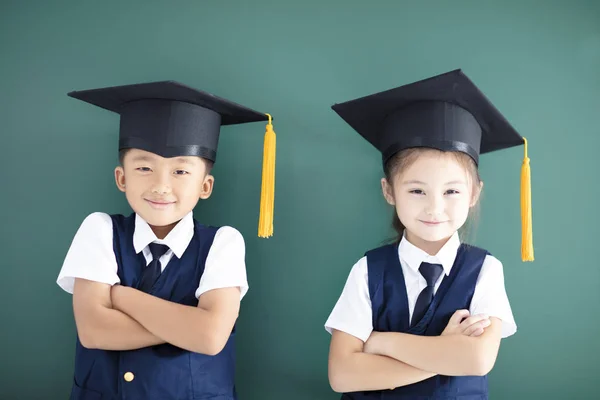 快乐男孩和女孩在毕业帽站立在黑板之前 — 图库照片