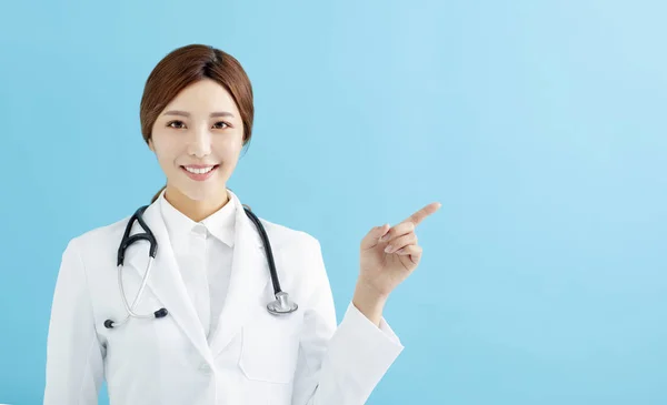 Lächelnde Ärztin Zeigt Mit Dem Finger Auf Blauem Hintergrund — Stockfoto