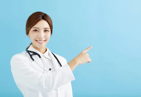 Lächelnde Ärztin Zeigt Mit Dem Finger Auf Blauem Hintergrund — Stockfoto