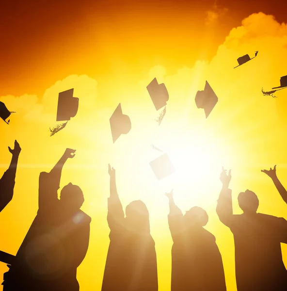 Estudiantes felices lanzando gorras de graduación en el aire — Foto de Stock