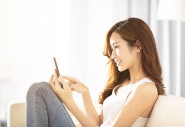 oturma odasında akıllı telefon kullanan genç kadın