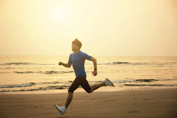 Молодой человек бежит по пляжу на закате — стоковое фото