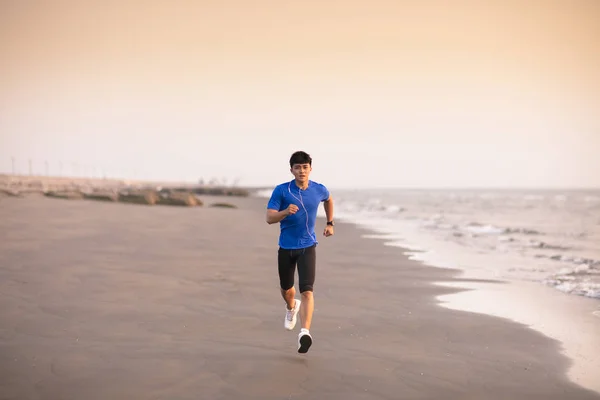 Mladý muž, který běží na pláži při západu slunce — Stock fotografie