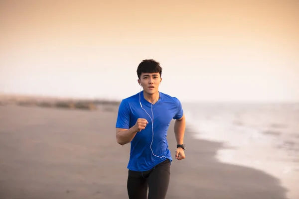 Молодой человек бежит по пляжу на закате — стоковое фото