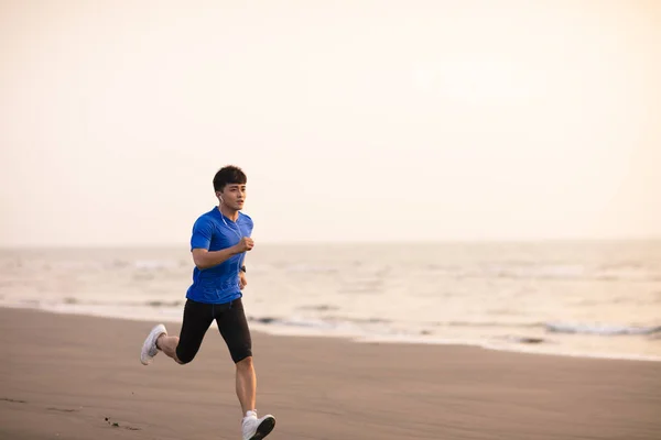 Jeune homme courir sur la plage au coucher du soleil — Photo