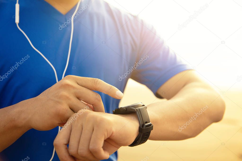 young Man running on beach and checking Heart Rate Monitor 