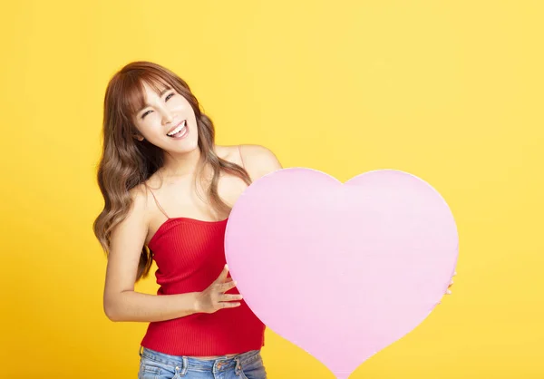 Sarı arka plan üzerinde izole pembe kalp tutan mutlu kadın — Stok fotoğraf
