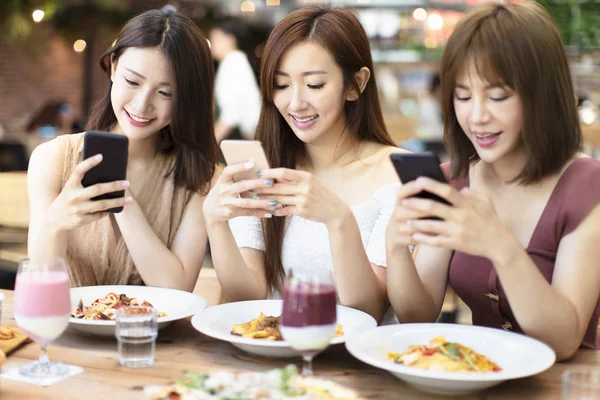 Amis heureux dîner et regarder le téléphone intelligent à restaure — Photo