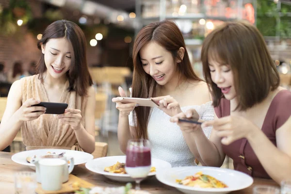 Šťastné přítelkyně večeřet a dívat se na chytrého telefonu z restaurace — Stock fotografie