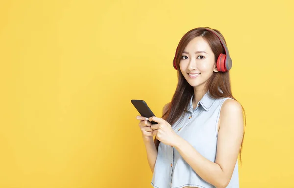 Mladá usměvavá žena držící sluchátka a mobil — Stock fotografie