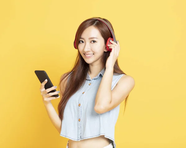 Jonge glimlachende vrouw met koptelefoon en mobiele telefoon — Stockfoto