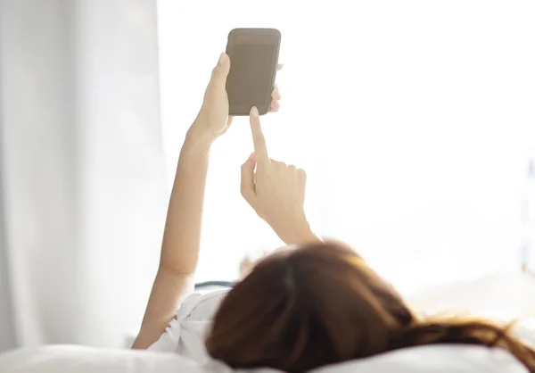 Mujer en la cama y la comprobación de aplicaciones con smartphone —  Fotos de Stock