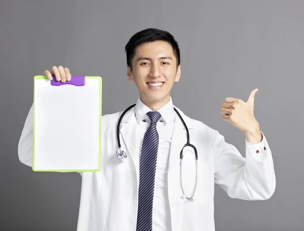 Jeune médecin masculin tenant un presse-papiers et montrant pouces vers le haut — Photo