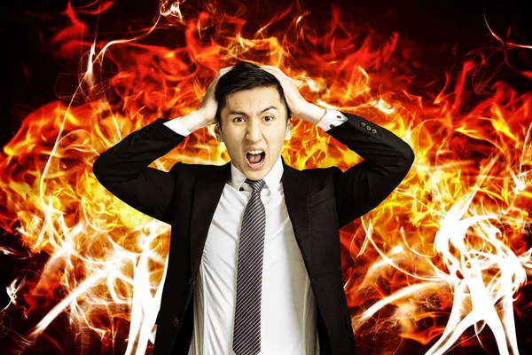 Angry young business man with burning fire background — Stock Photo, Image