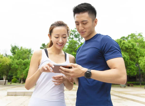 Joven pareja de fitness vistiendo ropa deportiva y mirando smartphon —  Fotos de Stock