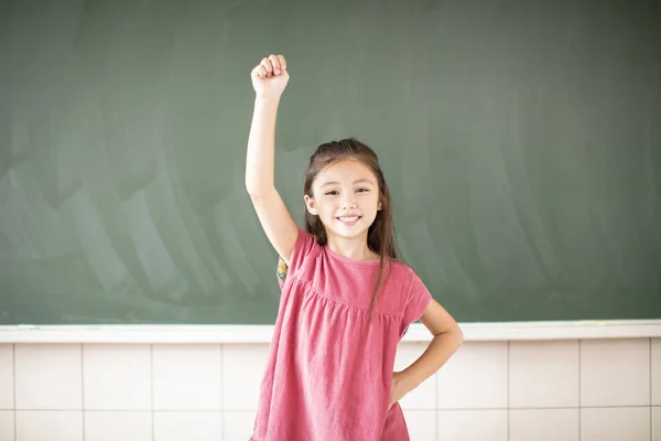 Happy little girl standing against chalkboard background — Stock Photo, Image