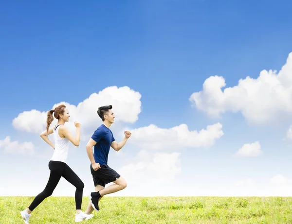 Sidovy av ungt par som springer på gräset — Stockfoto