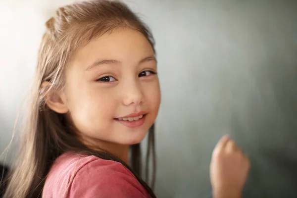 Little girl smiling in front of chalkboard — Stock Photo, Image