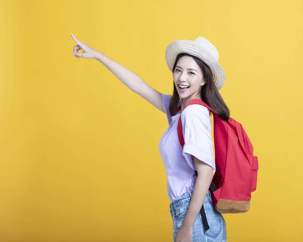 Smiling and pointing young woman with backpack standing on yello — Stock Photo, Image