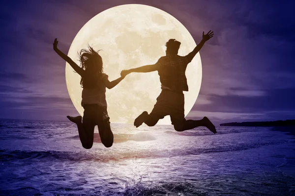 Pareja joven saltando en la playa y viendo la luna. Celebra Mi —  Fotos de Stock