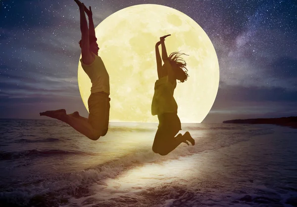 Pareja joven saltando en la playa y viendo la luna. Celebra Mi — Foto de Stock