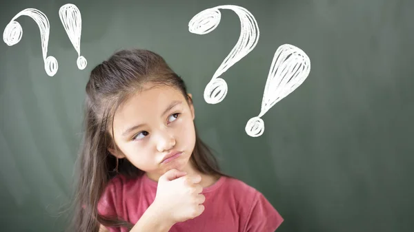 Kleines Mädchen steht mit Fragezeichen an Tafel — Stockfoto