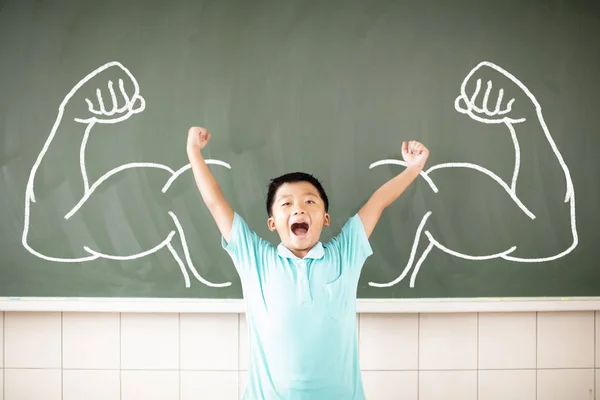 Happy school boy with strong pose and standing against chalkboard Stock Image