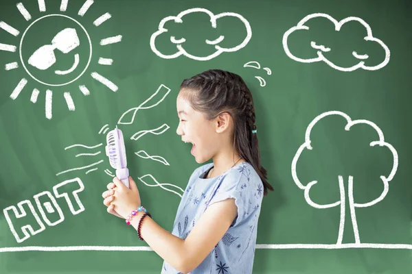 Chica de la escuela feliz sosteniendo ventilador y de pie contra pizarra — Foto de Stock