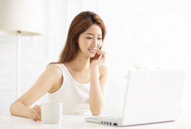 oturma odasında dizüstü bilgisayar kullanarak gülümseyen genç kadın